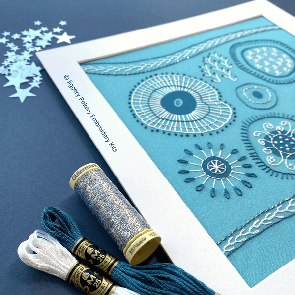 Silver, dark turquoise and white threads shown with a close-up of the finished abstract embroidery on a navy blue background