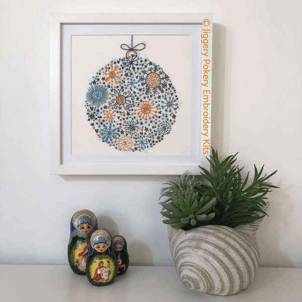 Scandinavian Christmas embroidery framed on wall, shown with Russian dolls and plant for scale