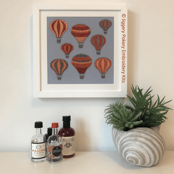 Hot air balloons embroidery kit in white frame shown with miniature gin bottles and plant for scale