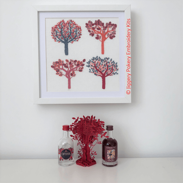 Autumn trees embroidery pattern framed hanging on wall, shown with miniature gin bottles for scale