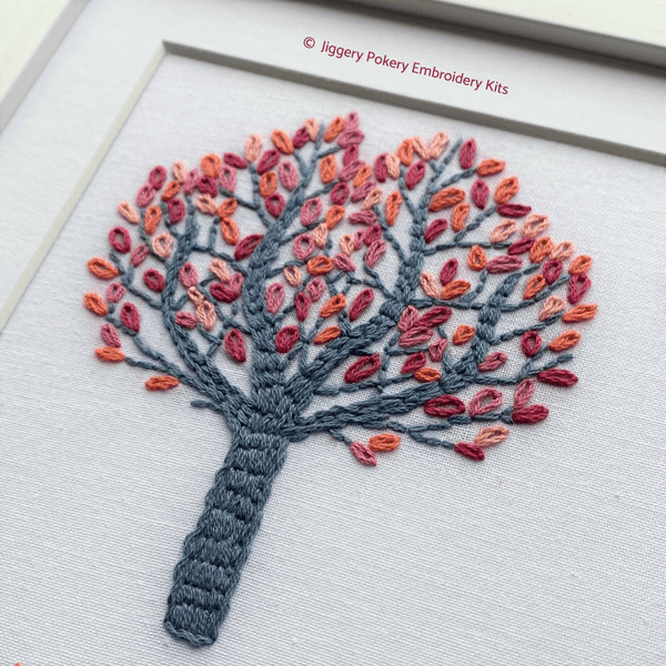 Autumn embroidery close-up of top left tree stitched in lazy daisy in red, orange and pink with a dark grey trunk