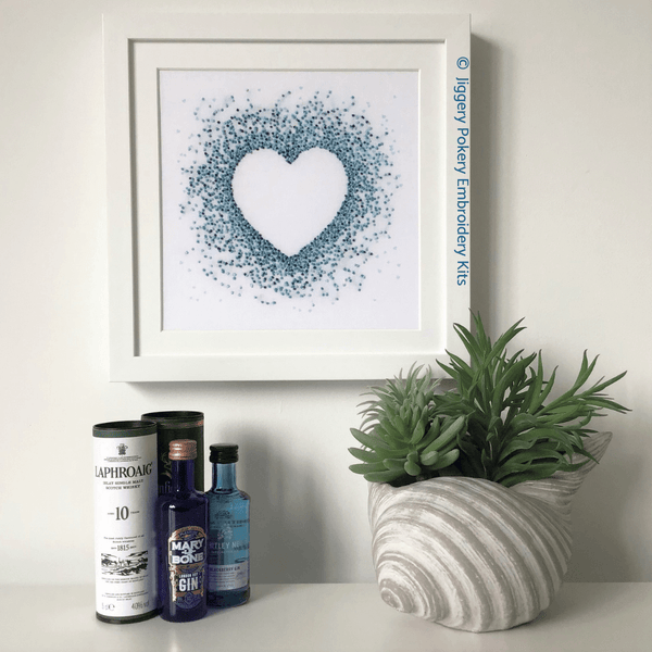 Blue hearts embroidery in frame on wall shown with miniature gin bottles for scale