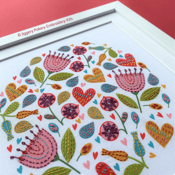Summer embroidery design of brightly coloured flowers and hearts mounted on red background