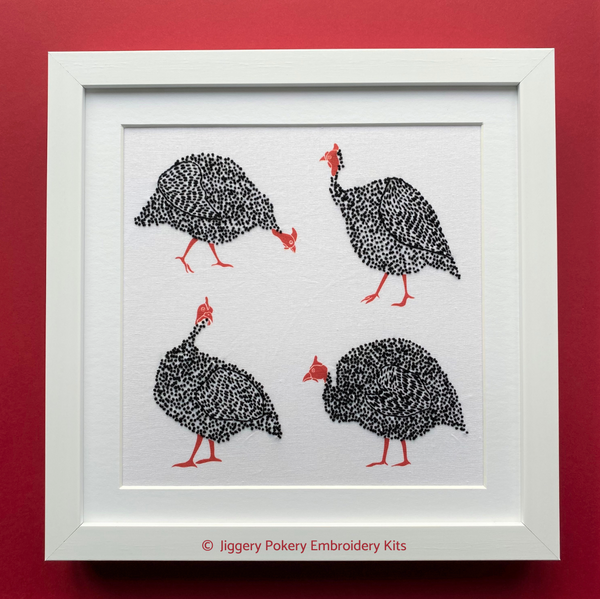 Guinea fowl embroidery kit in white mount and framed, shown on red background
