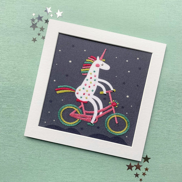 Unicorn hand embroidery pattern by Jiggery Pokery  mounted on green background with silver stars