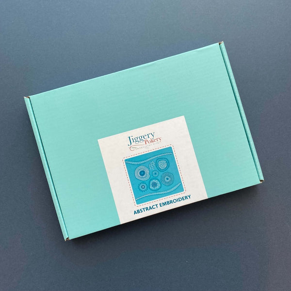Abstract embroidery kit in a turquoise mailing box with a label showing the embroidery design on the outside