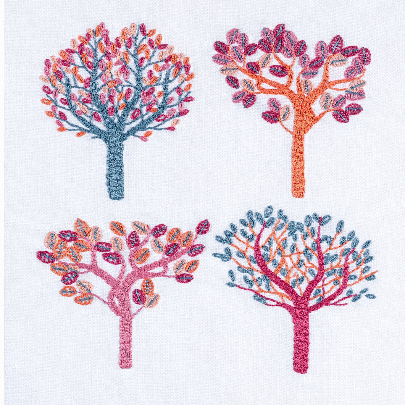 Autumn embroidery showing four trees using non-traditional DMC thread colours of salmon pink, air force blue, crimson, flame and pink.