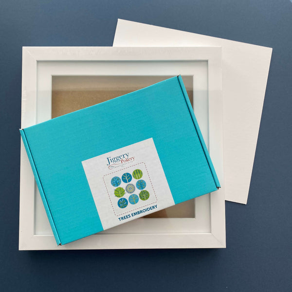 Blue and green trees embroidery kit and square white frame with a piece of mountboard cut to size