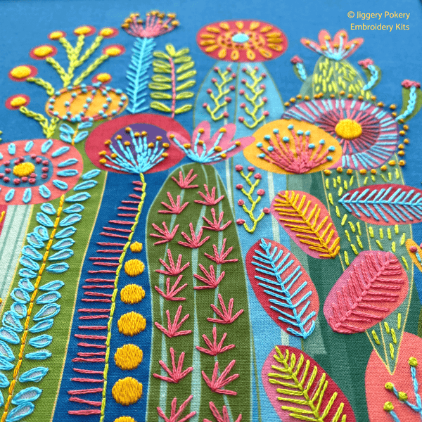 Close-up of stitching in bright pink, green, blue and yellow on a blue background for Jiggery Pokery's cactus embroidery kit