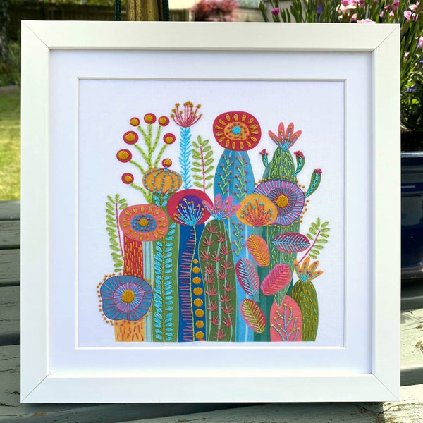 Cactus embroidery design on white fabric shown in a square white frame outdoors on a garden table