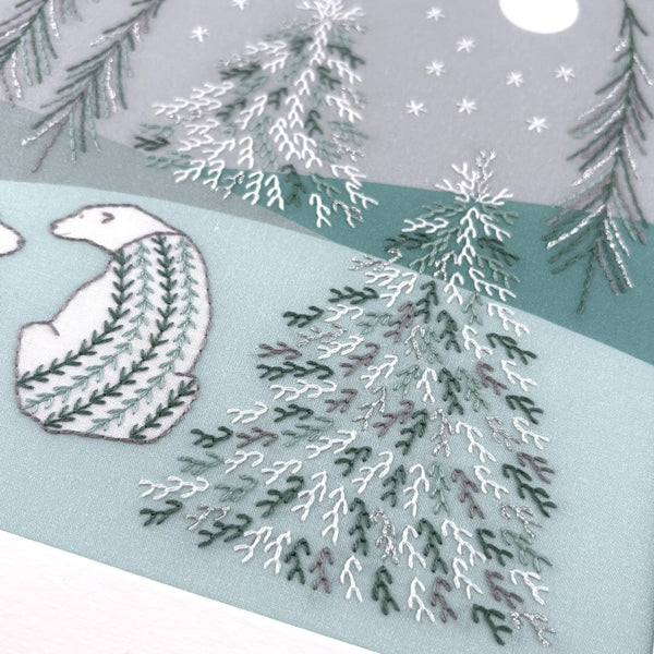 A close-up of one of the winter trees and a polar bear stitched in white, grey, silver metallic and green threads. 