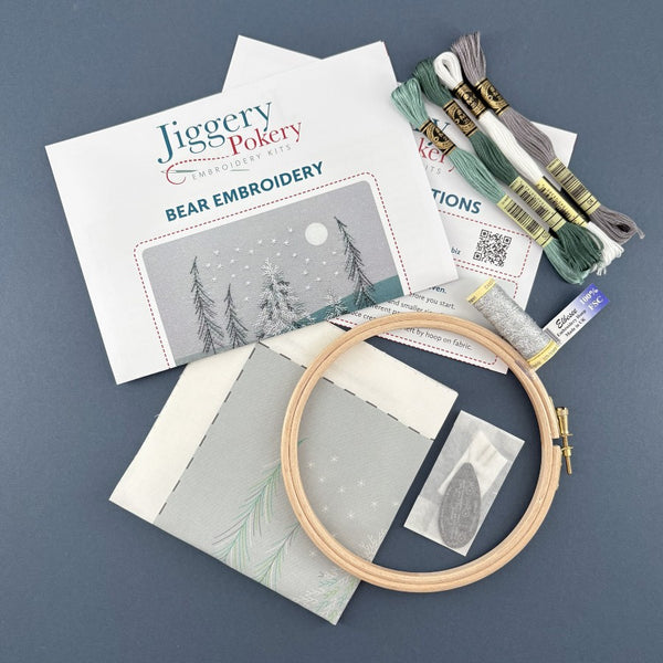 Embroidery kit containing a wooden hoop, DMC embroidery threads, Gutermann silver metallic effect thread, needles and a needle threader in a bag, fabric with the bear embroidery design printed on it plus instructions.