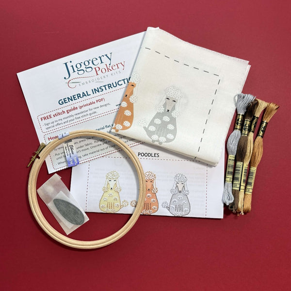 The poodles embroidery kit contains a wooden embroidery hoop, a needle threader and two needles in a bag, fabric with the poodle pattern printed onto it in colour, 4 skeins of DMC threads plus general and stitch instructions