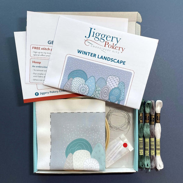 Contents of winter embroidery kit shown in a turquoise mailing box