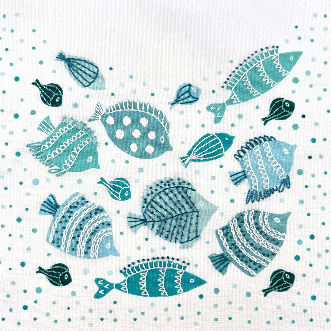 Fish embroidery kit creates a shoal of teal, green and blue fish decorated with simple embroidery stitches. The embroidery is done on top of a background of printed bubbles.