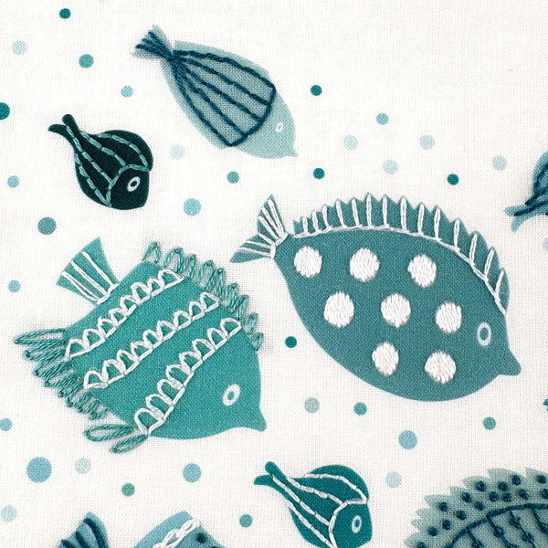 Close-up of the middle fish in the fish embroidery pattern. One fish is dark green and the other is lighter green, both with white stitching on top.