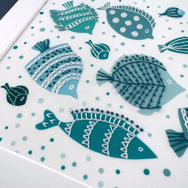 Close-up photo of some of the fish in the embroidery design. The fish are blue, light green and dark green, mostly stitched with white embroidery thread.