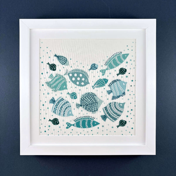 The completed fish embroidery pattern is shown with a white mount in a square white frame on a navy blue background.