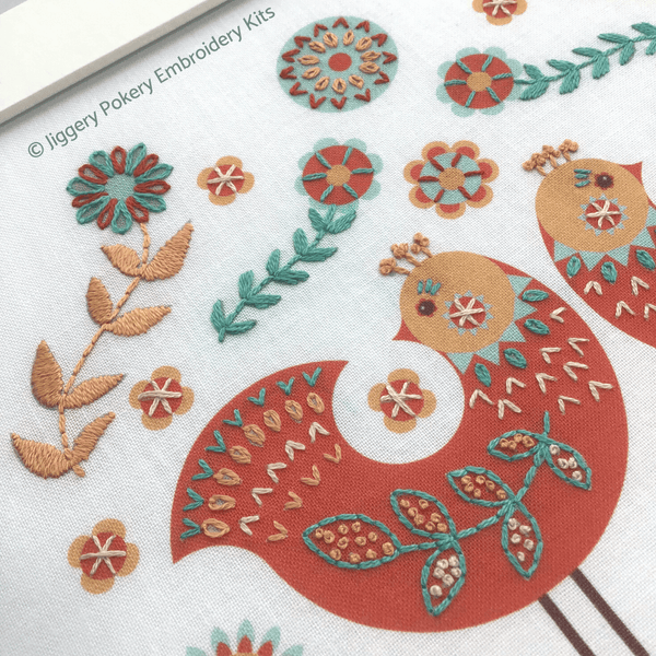 Folk art embroidery showing close-up of one red bird with pale orange, cream, red and teal stitching