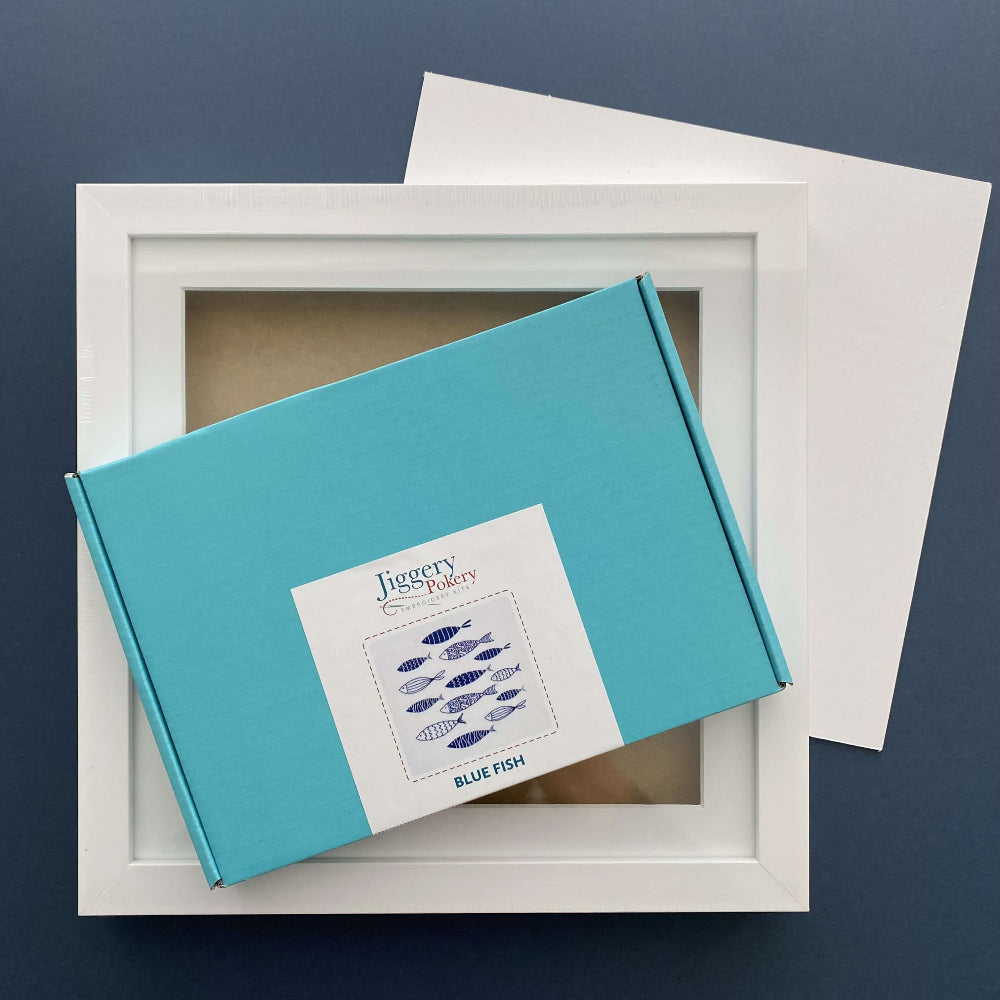 Blue fish embroidery kit and a square white frame with a piece of mountboard cut to size