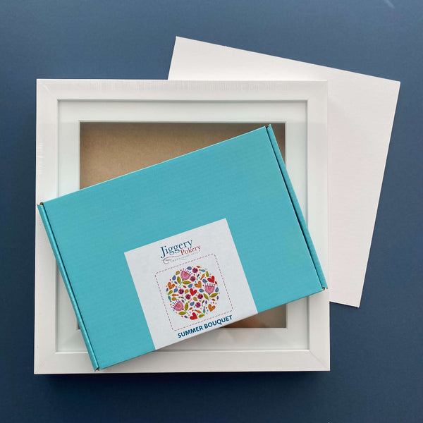 Multicoloured floral embroidery kit with a square white frame and a piece of mountboard cut to size