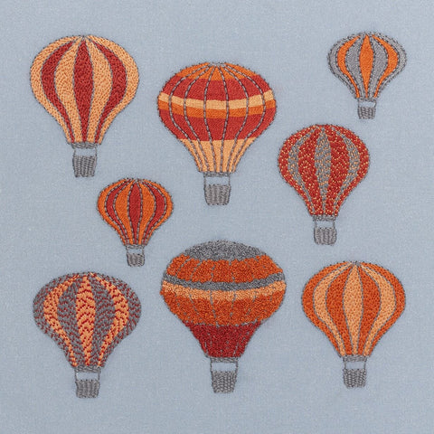 Embroidery kit showing a group of hot air balloons stitched in ruby red, apricot, orange and grey drifting on a dark grey sky