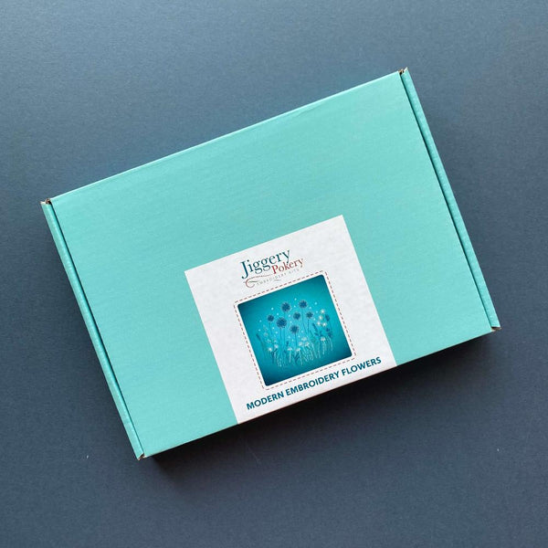 Modern embroidery flowers kit in a teal mailing box with a label showing the contents of the kit.