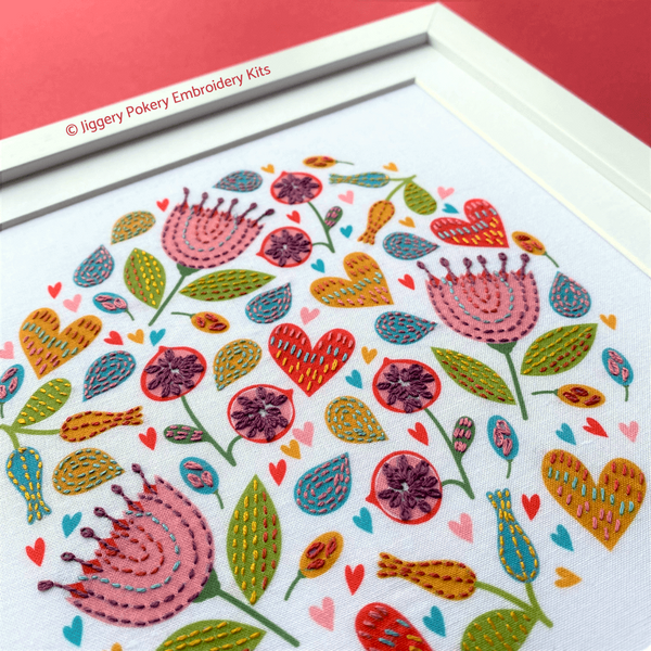 Flower embroidery pattern showing pink flowers, red and yellow hearts and green leaves, shown on a red background