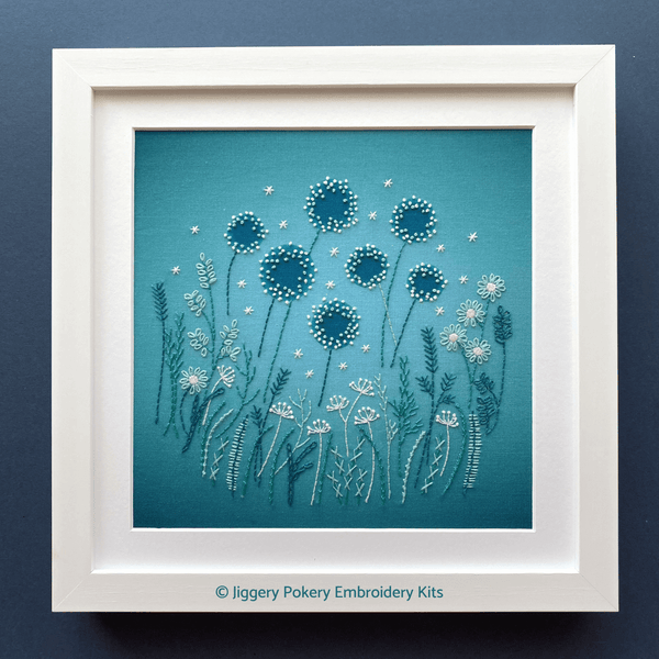 Modern flowers embroidery kit mounted in a square white frame, shown on a navy blue background.