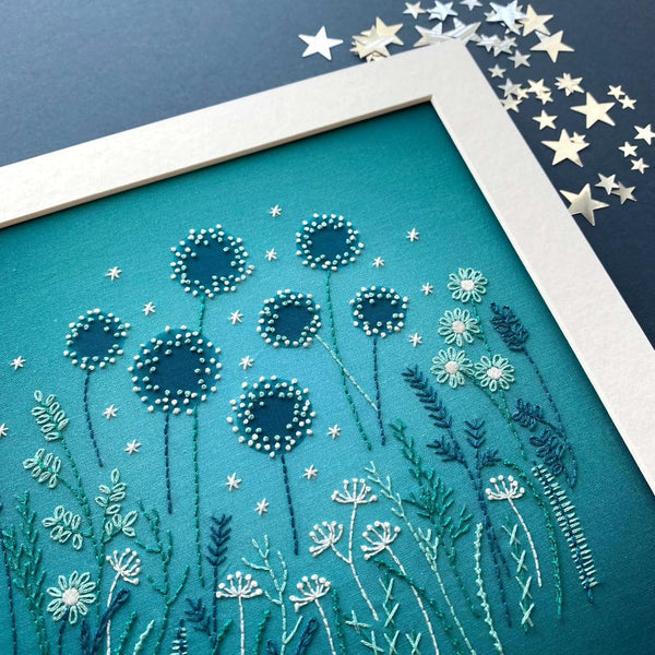 A close-up of the dandelion heads on the modern embroidery flowers pattern. Shown on a navy blue background with silver stars.