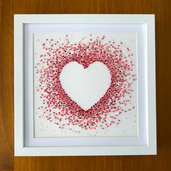 Pink hearts embroidery design mounted in a square white frame shown on a wood background