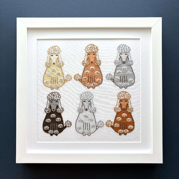 Completed poodles embroidery mounted in a square white frame, shown on a dark blue background