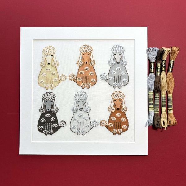 Poodles embroidery in a square white mount with 4 sets of DMC threads, shown on a dark red background