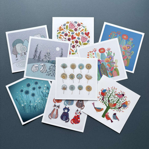 Collection of colourful printed  greeting cards featuring 9 different Jiggery Pokery embroidery designs, shown on a dark blue background.