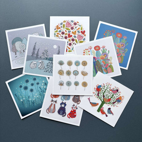 Collection of colourful printed  greeting cards featuring 9 different Jiggery Pokery embroidery designs, shown on a dark blue background.