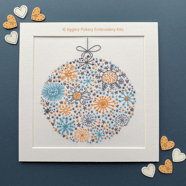 Festive ball Christmas embroidery kit shown on dark blue background with orange and white hearts