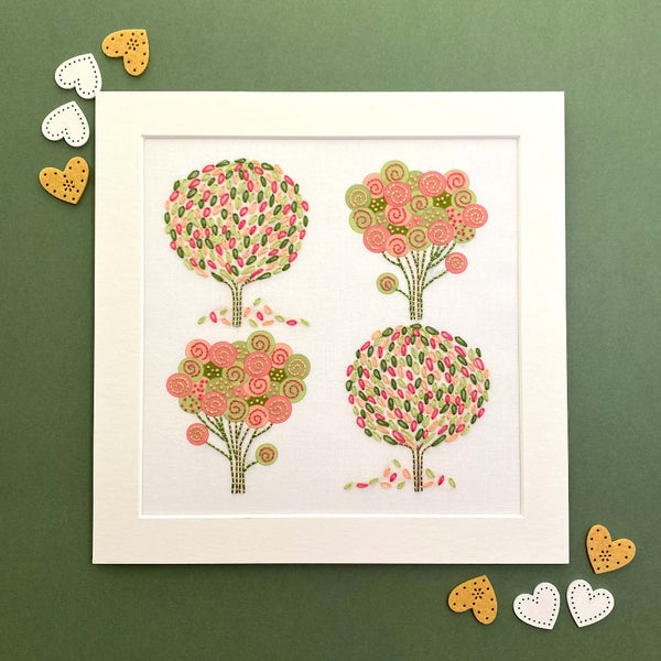 Spring embroidery kit completed and in a white mount, shown with hearts on a green background