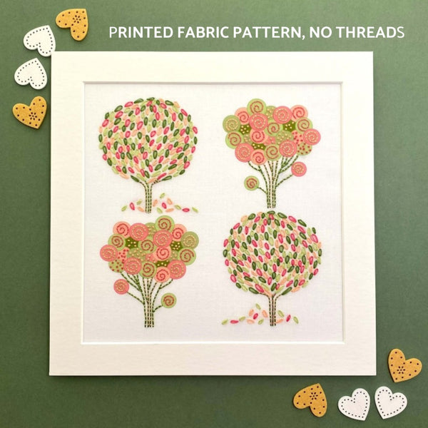 A group of 4 Scandinavian style trees in pink, green, peach and dark green. Shown in a square white mount on a dark green background with hearts at the corners