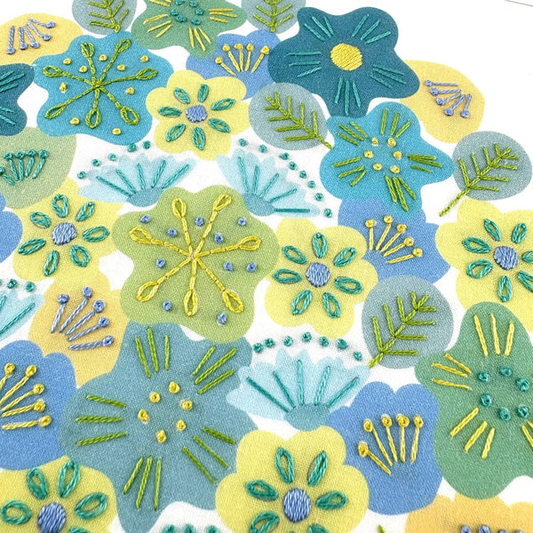 A close-up image of blue, yellow, green, teal and turquoise flowers with simple embroidery stitches done on top of the pre-printed fabric.