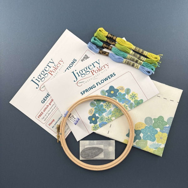 Spring flowers embroidery kit contents: a wooden hoop, needles and needle threader in a bag, 4 skeins of DMC threads, fabric with the pattern printed on it plus general instructions and stitch instructions.