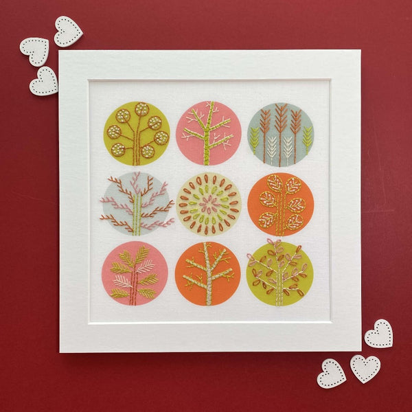Pink and orange trees embroidery pattern shown on a red background with white heart decorations