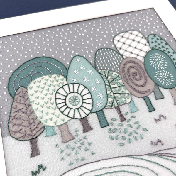 Embroidered design of winter trees on fabric with a grey background