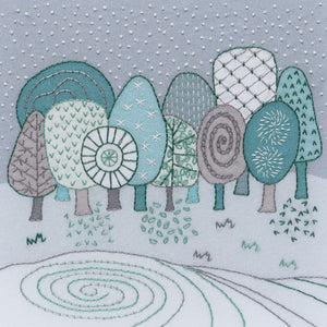 This embroidery kit creates a winter landscape of trees and a frozen lake. The stitching is done in silver metallic thread and DMC threads in 