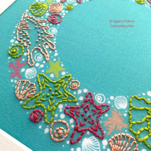 Close-up of seashells embroidery pattern showing green and pink starfish with shells, seaweed and bubbles