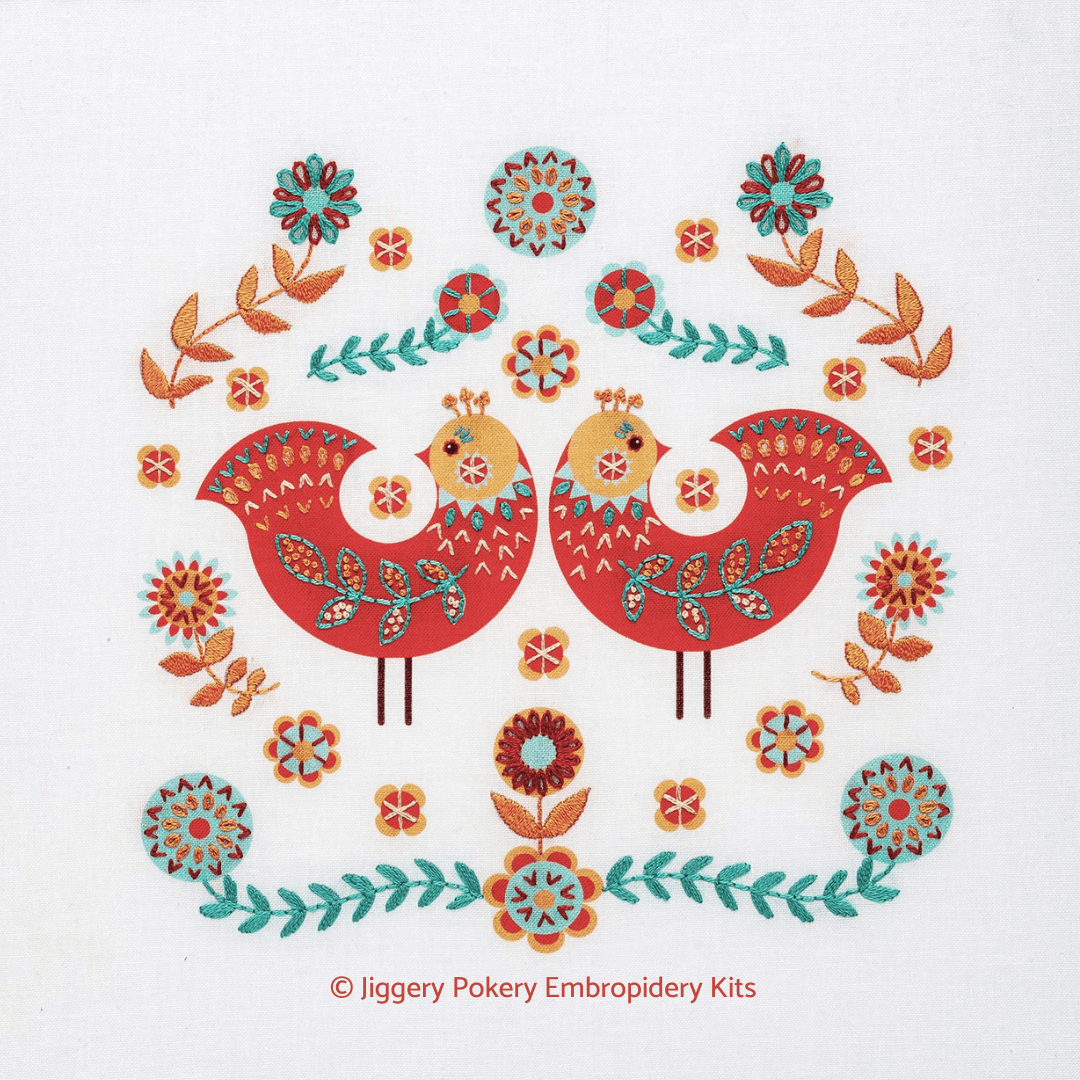 Folk art birds embroidery kit showing two red birds surrounded by flower motifs in apricot and turquoise