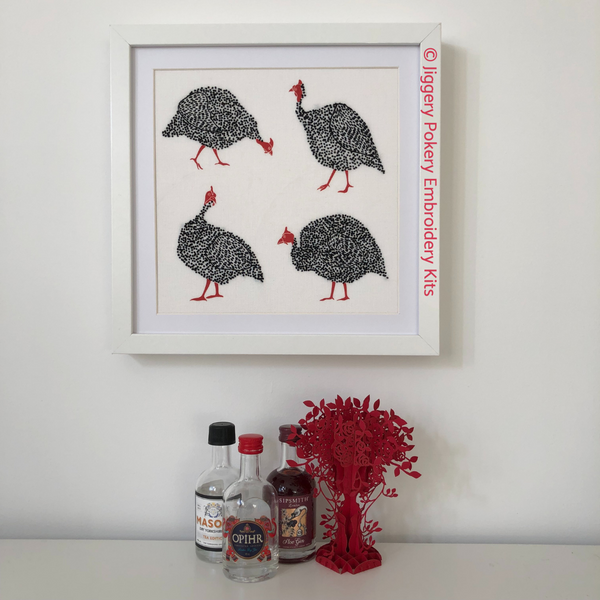 Guinea fowl bird embroidery pattern framed on wall shown with miniature gin bottles for scale