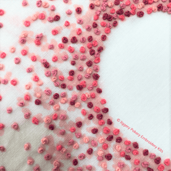 Pink hearts embroidery hoop close-up showing French knots stitched over printed pink hearts background